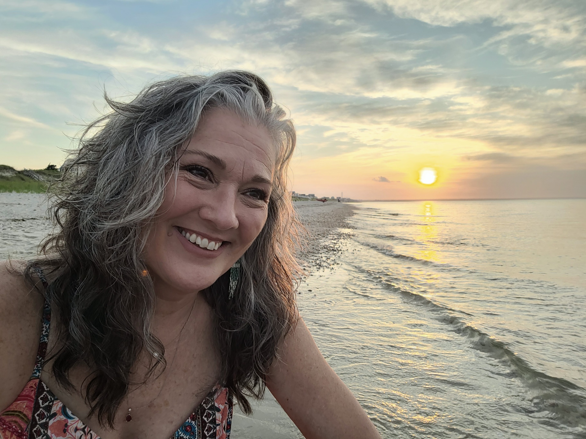 Founder smiling at golden hour with the sun setting over the ocean behind her