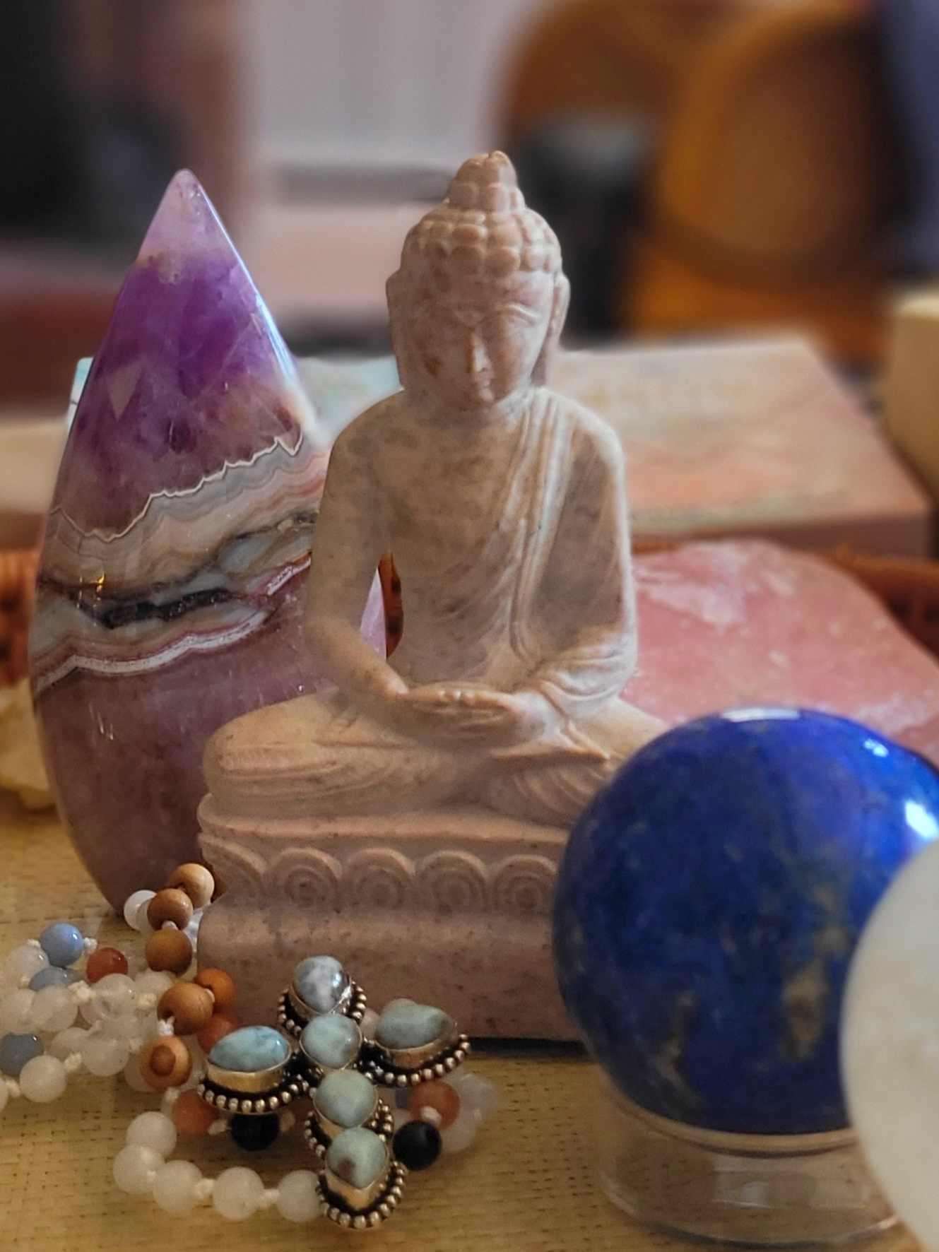 An altar with a stone Buddha, amethyst, lapis sphere, mala beads, and a larimar cross